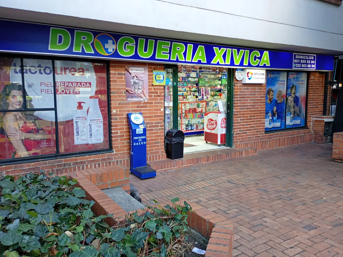 Fachada de la sede Tejares del Norte: aviso azul con la palabra Droguería Xivica en verde sobre la entrada, en un local de ladrillo con vitrinas a los lados
